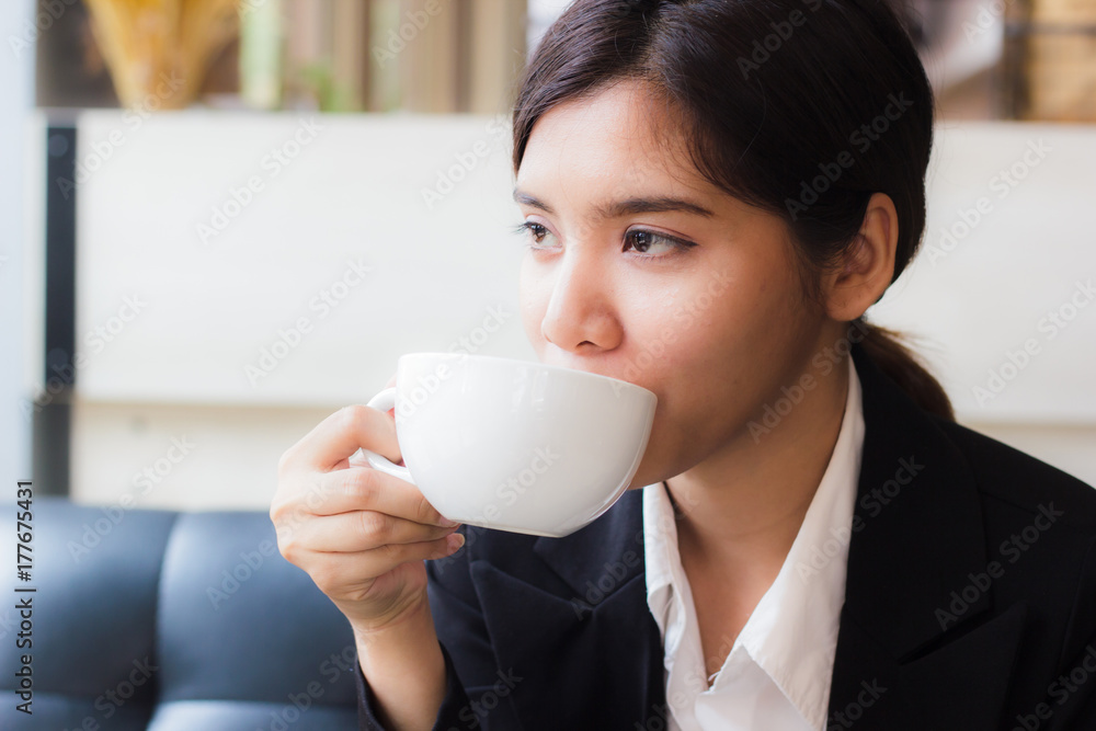 Asian business woman relaxing in coffee shop with hot coffee. Copy space. Coffee is a relaxing place for everyone today. Hand holding white cup of coffee. Smiling asian businesswoman sit by the window Asian business woman relaxing in coffee shop with hot coffee. Copy space. Coffee is a relaxing place for everyone today. Hand holding white cup of coffee. Smiling asian businesswoman sit by the window