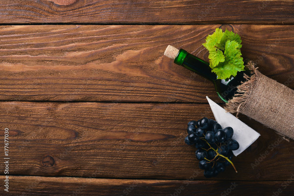 A bottle of wine and grapes. On a wooden background. Top view. Free space for your text. A bottle of wine and grapes. On a wooden background. Top view. Free space for your text.
