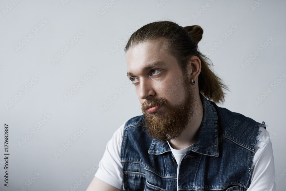 Fototapeta premium Studio shot of attractive fashionable European student with bushy beard and hair bun rolling eyes while feeling bored during dull tiresome lecture at college. Human facial expressions and emotions