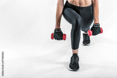 Low section of a sportswoman holding pink dumbbells wears black leggins o nwhite isolated background