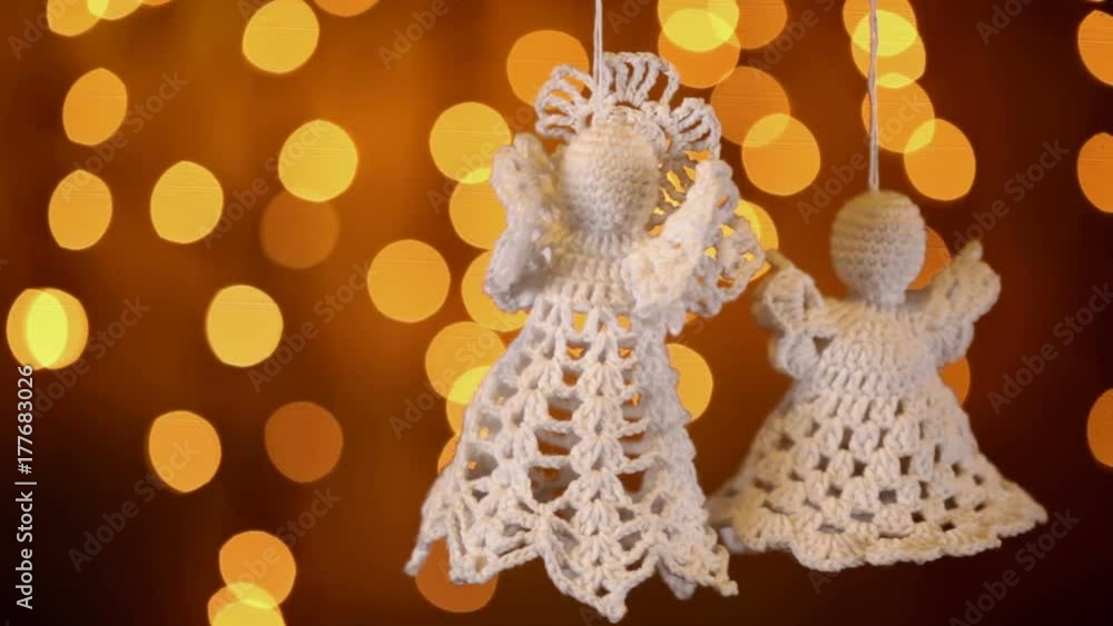 Two crochet christmas angel decorations hanging in front of golden blurry xmas lights - static camera Two crochet christmas angel decorations hanging in front of golden blurry xmas lights - static camera