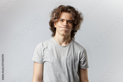 Human facial expressions, feelings, emotions and reaction. Frustrated sorrowful young man in casual grey t-shirt pursuing lips and blowing cheeks expressing sorrow, perplexity or disappointment photo