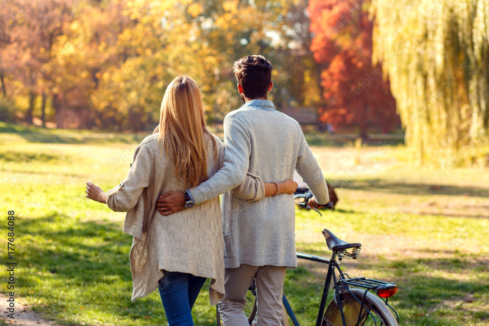 Back view of young couple with bicycle walking in park on sunny autumn day. Back view of young couple with bicycle walking in park on sunny autumn day.