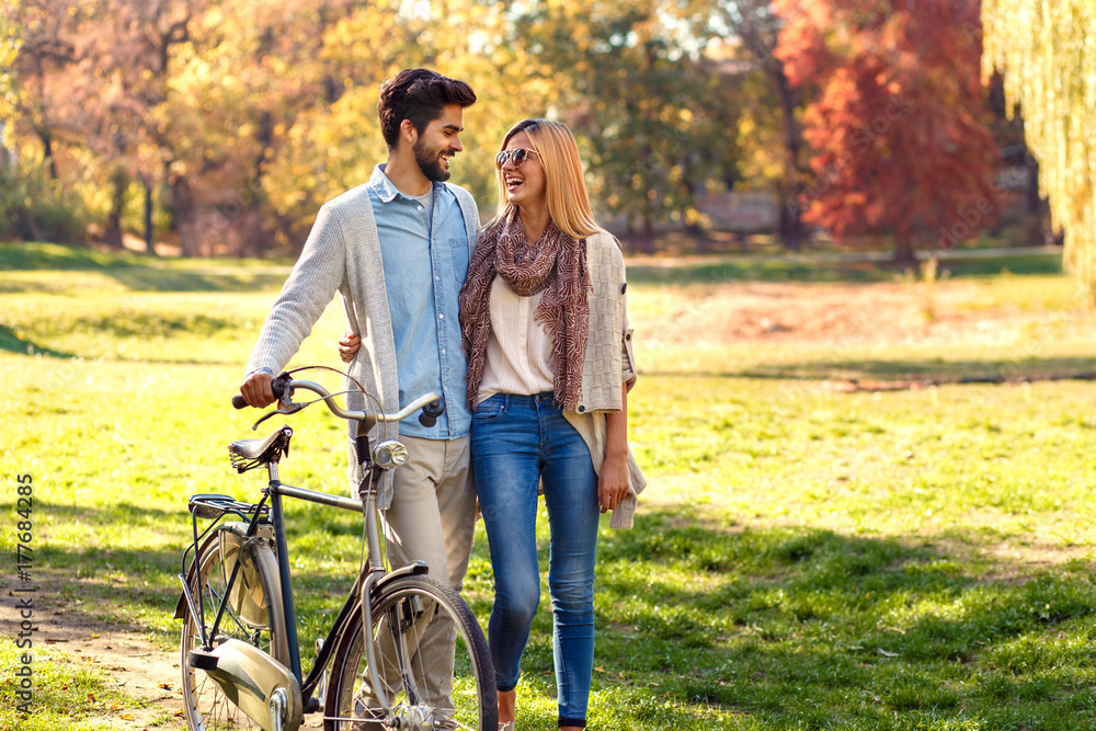 Young couple with bicycle walking in park on sunny autumn day.