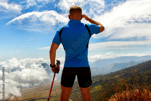 Sporty guy traveler in a blue t-shirt on a background of a beautiful sky with clouds in the mountains.