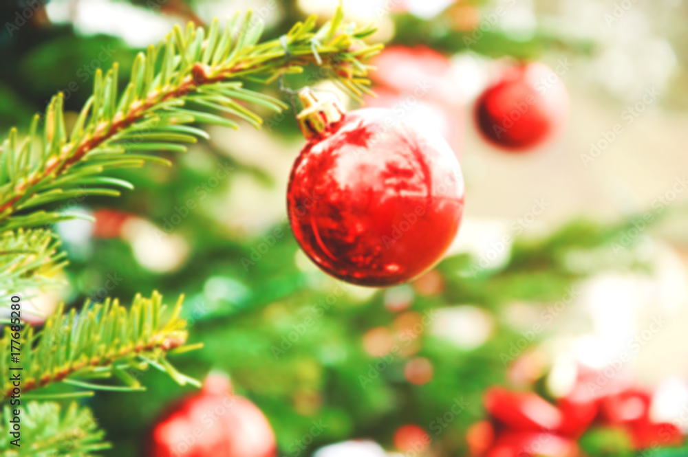 Blurry photo of Christmas tree outdoor. Reflection of trees in red Christmas ball.