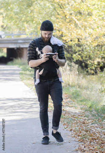 Millennial Dad with Baby in Carrier Outside Talking and Texting on a Beautiful Fall Day