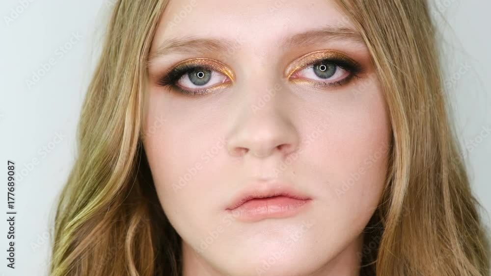 Close up portrait of beautiful young woman face with bright bronze make up looking at camera, then in front. Girl showing eye make-up Close up portrait of beautiful young woman face with bright bronze make up looking at camera, then in front. Girl showing eye make-up