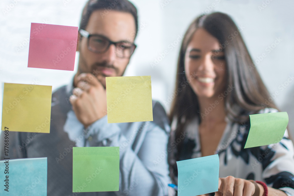Serious man looking at adhesive notes on glass wall with his female business colleague. Serious man looking at adhesive notes on glass wall with his female business colleague.