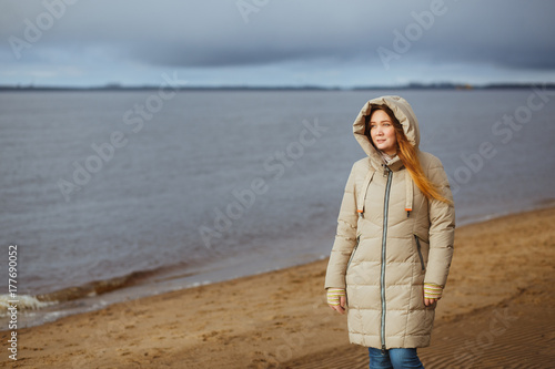 Beautiful woman in winter clothes standing by the river and looking to winter sunset. Seasonal  fashion and relationship concept