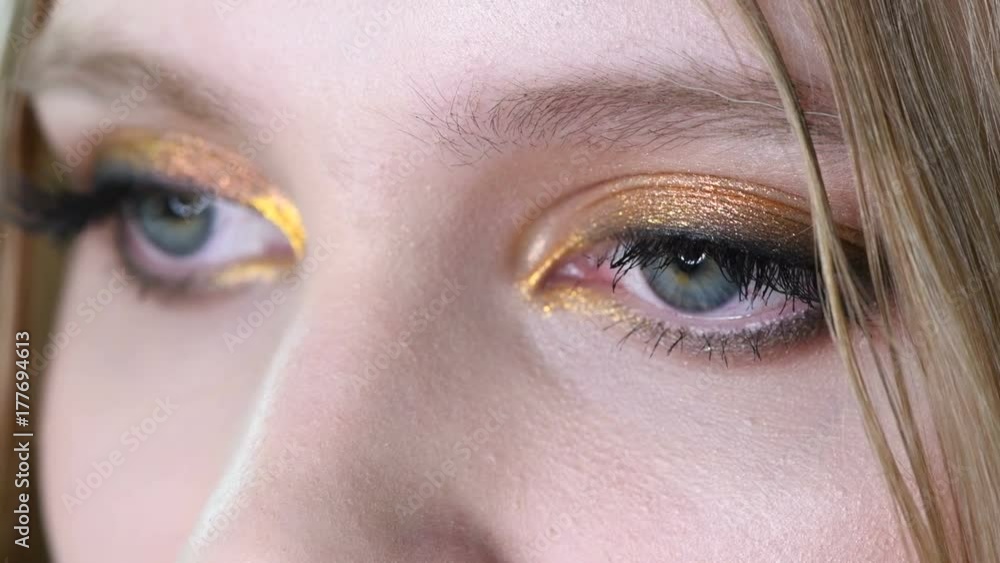 Close up view of blue woman eye with beautiful golden shades makeup. Classic make up. Perfect shape make-up and long lashes. Cosmetics and make-up. Closeup macro shot of fashion eyes visage Close up view of blue woman eye with beautiful golden shades makeup. Classic make up. Perfect shape make-up and long lashes. Cosmetics and make-up. Closeup macro shot of fashion eyes visage