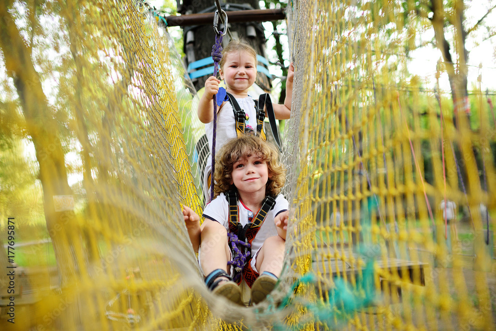 cute children - a boy and a girl in an adventure park are engaged in rock climbing or pass obstacles on the rope road. cute children - a boy and a girl in an adventure park are engaged in rock climbing or pass obstacles on the rope road.
