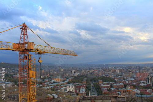 orange high construction crane against the background cityscape, of the blue sky and clouds