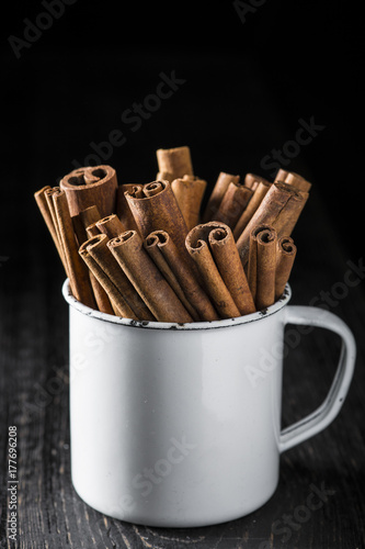 Taza de porcelana con palitos de canela en rama sobre fondo de madera negro photo