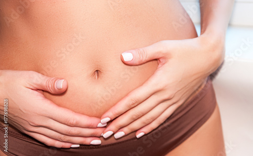 A tanned girl holds her hands to her stomach. IVF concept, pregnancy, digestion, health of the female reproductive system.