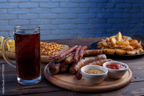 Appetizing beer snacks set. Grilled sausages and baked potatoes served with spicy tomato sauce, whole grain mustard and dark beer, free space. Oktoberfest food, pub concept