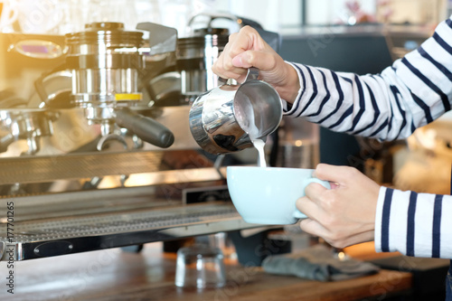 Women barista hand pouring milk into coffee cup at cafe counter, making coffee, latte art, food and drink concept