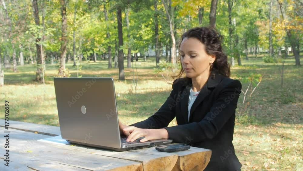 Business woman with laptop throws the phone. A woman in a business suit in a park is throwing a phone. Business woman with laptop throws the phone. A woman in a business suit in a park is throwing a phone.