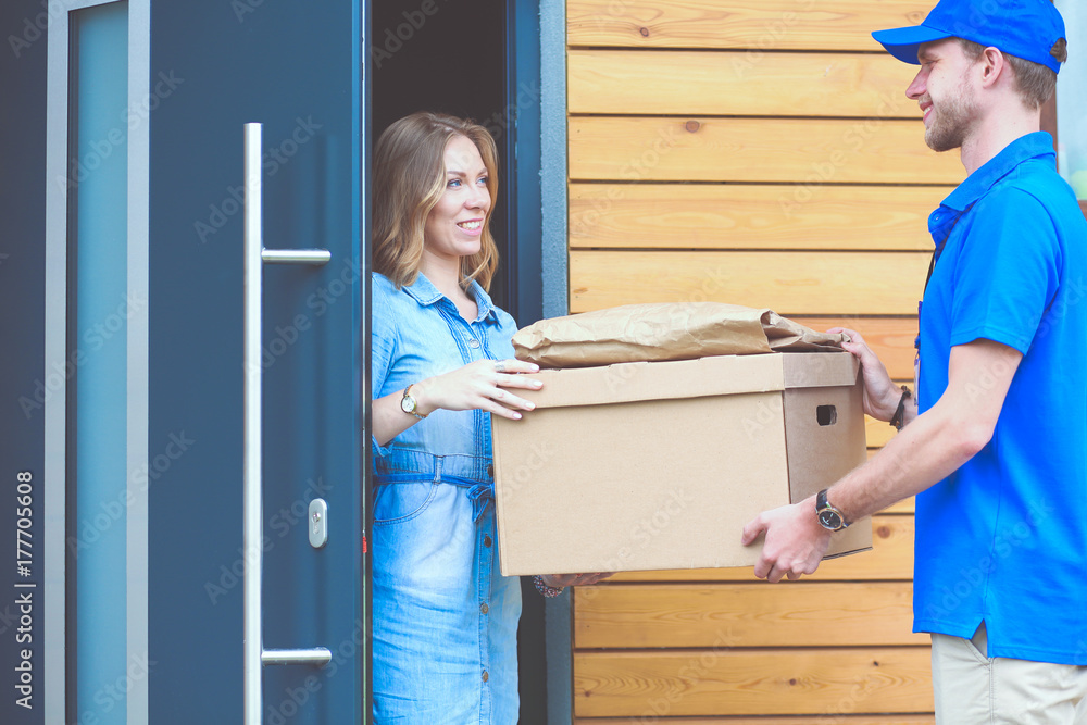 Smiling delivery man in blue uniform delivering parcel box to recipient - courier service concept. Smiling delivery man in blue uniform Smiling delivery man in blue uniform delivering parcel box to recipient - courier service concept. Smiling delivery man in blue uniform