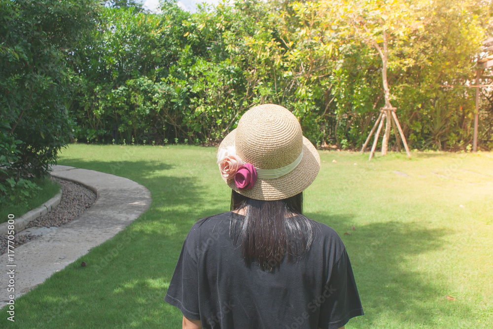 Relaxation Concept : Asian woman wearing weave hat and walking on footpath in outdoor garden with green natural and sunlight background.