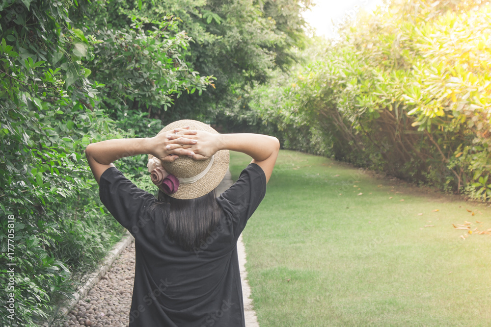 Relaxation Concept : Asian woman wearing weave hat and walking on footpath in outdoor garden with green natural and sunlight background.
