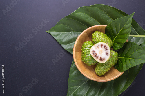Fruit of Great morinda (Noni) or Morinda citrifolia tree and green leaf on black stone board photo