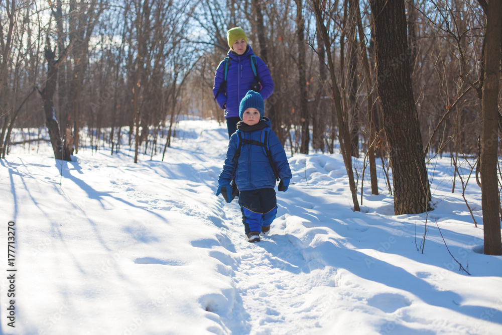 The boy walks with his mother through the wood in the winter.