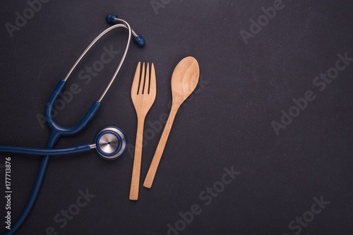 Blue doctor Stethoscope and set of spoon, fork and wooden dish on black stone board. Food and healthy check up,Eating control or diet concept