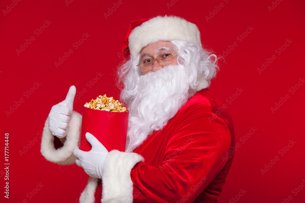 Naklejka premium Traditional Santa Claus watching TV, eating popcorn. Christmas. Red background. emotions fear surprise
