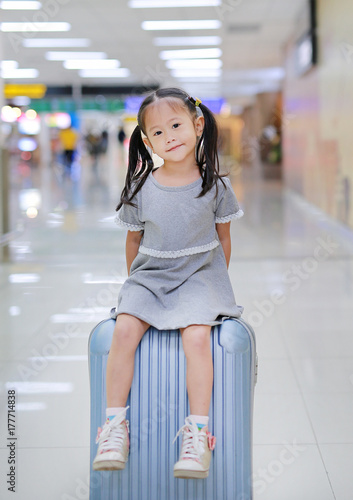 Cute little girl sitting on suitcase at the airport.