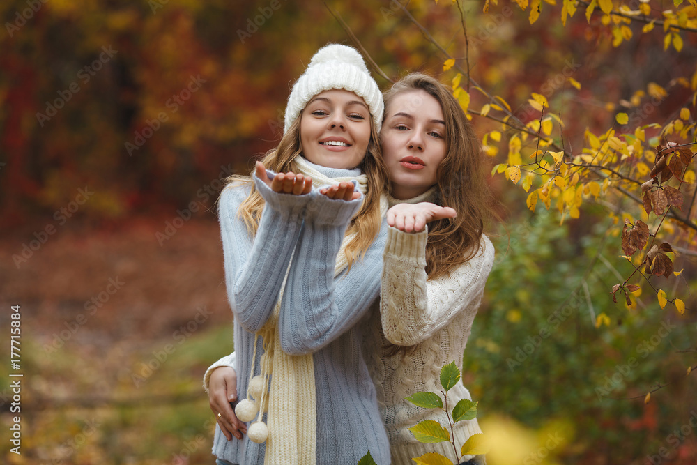Beautiful girlfriends on the autumn background having fun. Cheerful women in the fall time. Smiling girlfriends outdoors sending an airkiss Beautiful girlfriends on the autumn background having fun. Cheerful women in the fall time. Smiling girlfriends outdoors sending an airkiss