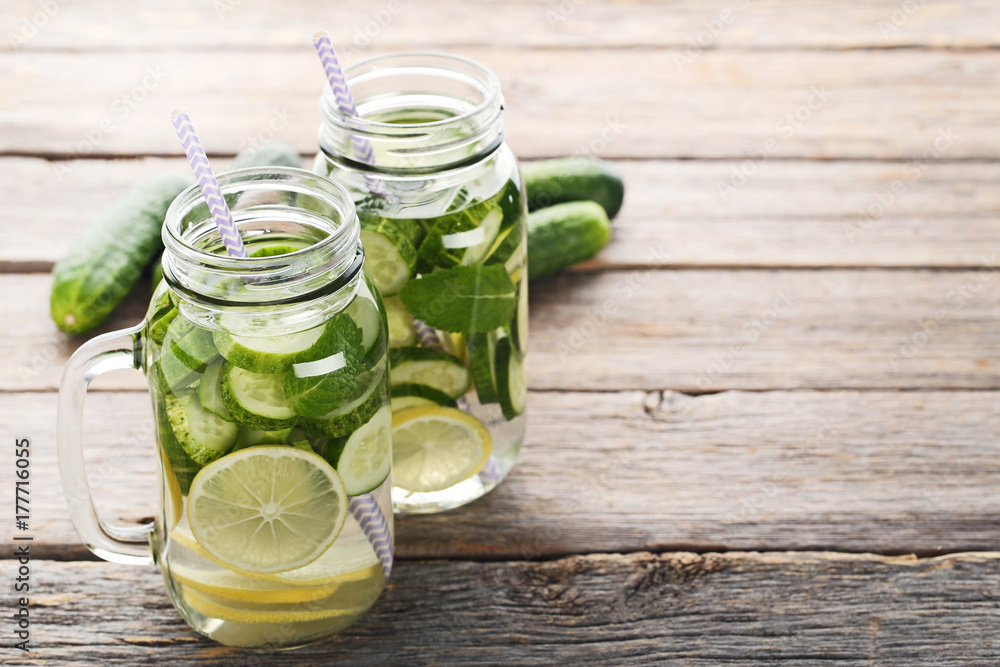 Lemonade with cucumbers, lemons and mint leafs in glass jars on wooden table Lemonade with cucumbers, lemons and mint leafs in glass jars on wooden table