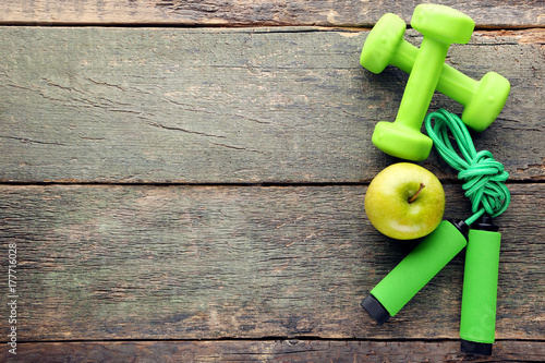 Green apple, skipping rope and dumbbells on wooden table