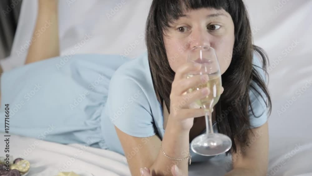 lonely young attractive woman lies on a bed in a bedroom, drinks champagne lonely young attractive woman lies on a bed in a bedroom, drinks champagne