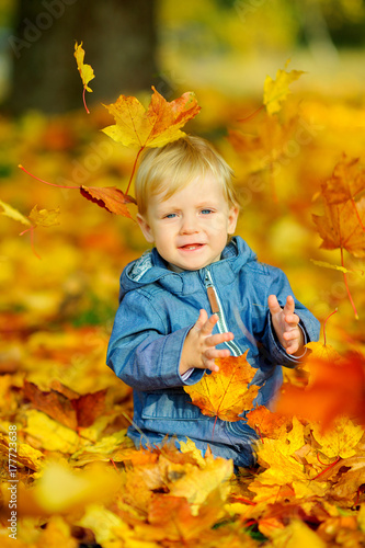 happy kid in a beautiful autumn park  playing and cheering under falling leaves.