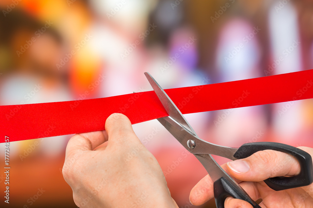 Fototapeta premium Hand with scissors cutting red ribbon - opening ceremony