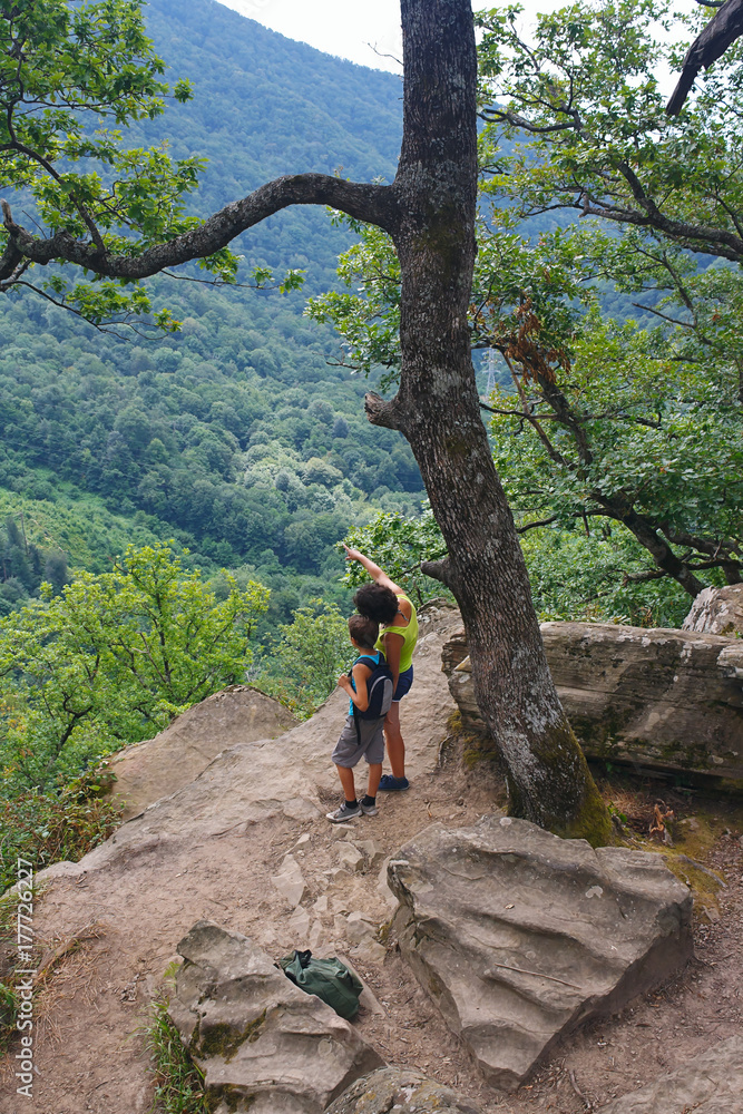 Mom and son tourists are looking from the high mountain to the view below