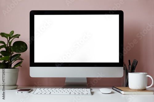 Mock up of white desktop with electronic devices, stationary items, cup of tea, copybook and decorative green plant over pinkish wall. Minimalistic modern workplace of student or freelancer