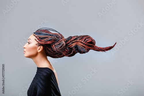 Fashion studio shoot of a mixed race woman with a creative colorful hairstyle in the form of a pigtail braided from dreadlocks in the technique of zizi. The concept of hairdressing art