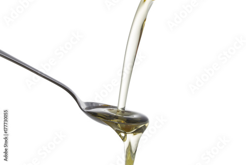 Olive oil poured from a bottle into a spoon isolated on white background