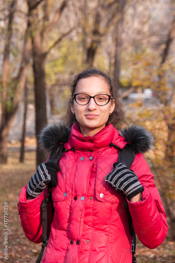 Beautiful girl in a red jacket with a backpack stands in the autumn forest Beautiful girl in a red jacket with a backpack stands in the autumn forest
