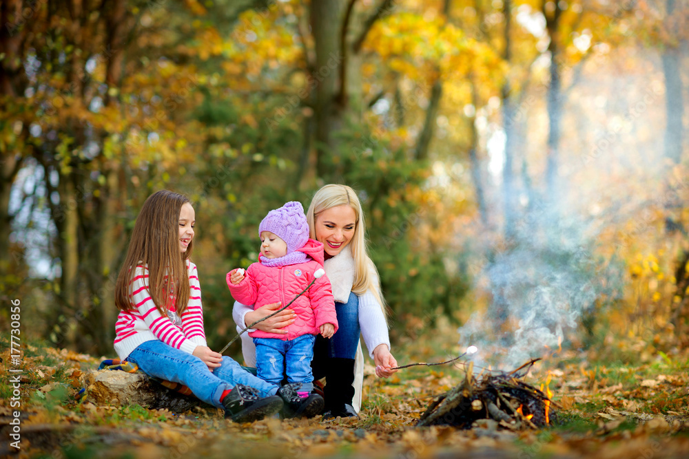 happy mother with two daughters in a beautiful autumn park, fry marshmallows at the stake. happy mother with two daughters in a beautiful autumn park, fry marshmallows at the stake.