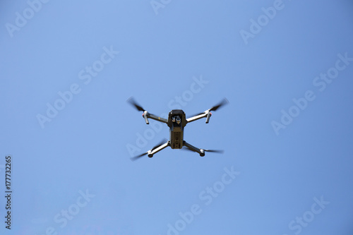 Small foldable drone flying viewed from below on a blue sky 