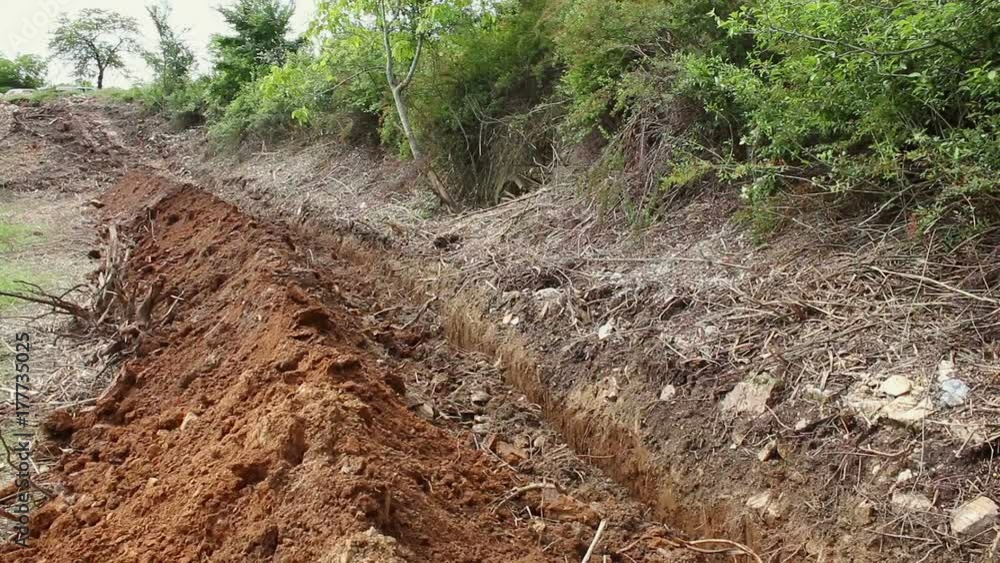 Excavator operating and digging soil for new electricity line. A backhoe tractor works on a construction site in open area green field. Excavator operating and digging soil for new electricity line. A backhoe tractor works on a construction site in open area green field.