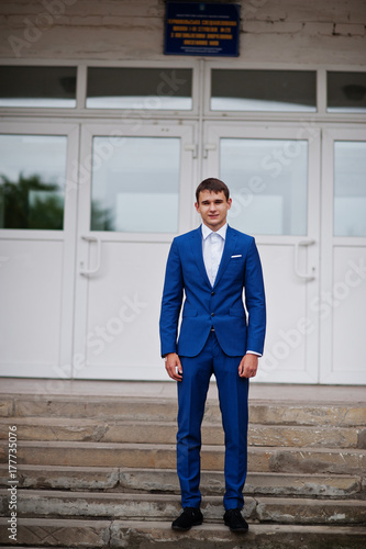 Portrait of a handsome high school graduate in stylish tuxedo posing on the stairs on the prom.