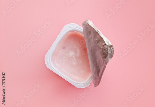 Opened strawberry yogurt or pudding  in white plastic cup on pink background with copy space.  Minimal style, flat lay, top view.