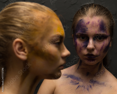 Portrait of couple attractive young woman with painted colorful faces. Standing and looking to camera. Dark background. © Yevgeniy Zateychuk