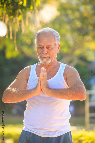 Grey Bearded Old Man in White Vest Shows Yoga Pose in Park