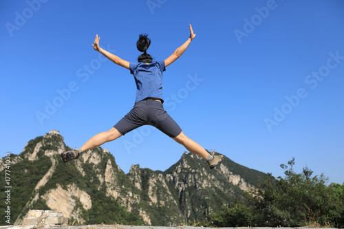 successful woman hiker jumping on mountain top