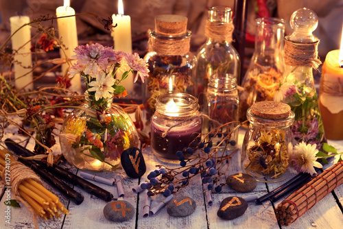 Rune stones, flowers and herbs on witch table in candle light